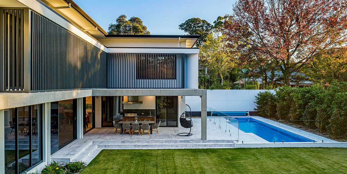 Modern home backyard â€“ characterised with vertical charcoal battens set off by a green lawn and blue pool