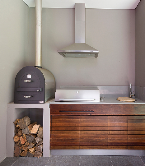 Outdoor kitchen with stainless steel bench, wooden cabinetry and a wood stove on the side