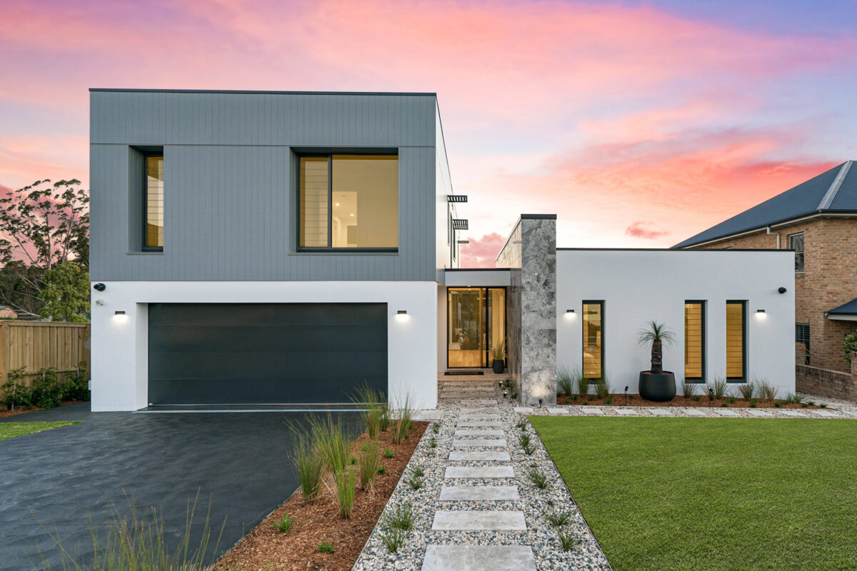 Street view of ultra modern grey/white/charcoal house, with a path leading up; set against a sunset