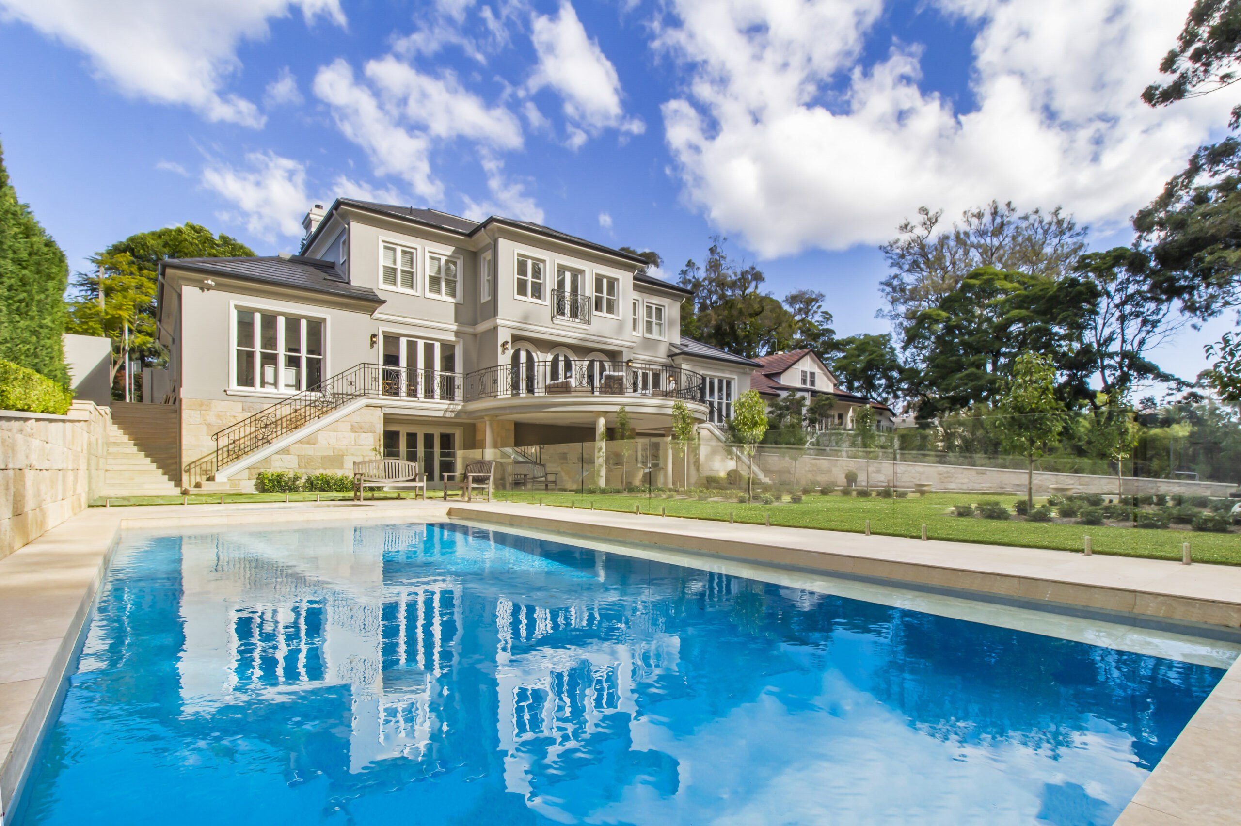 Pymble home in Provincial Style â€“ blue pool closeup with a grand, stately, provincial-style home rising up in the background