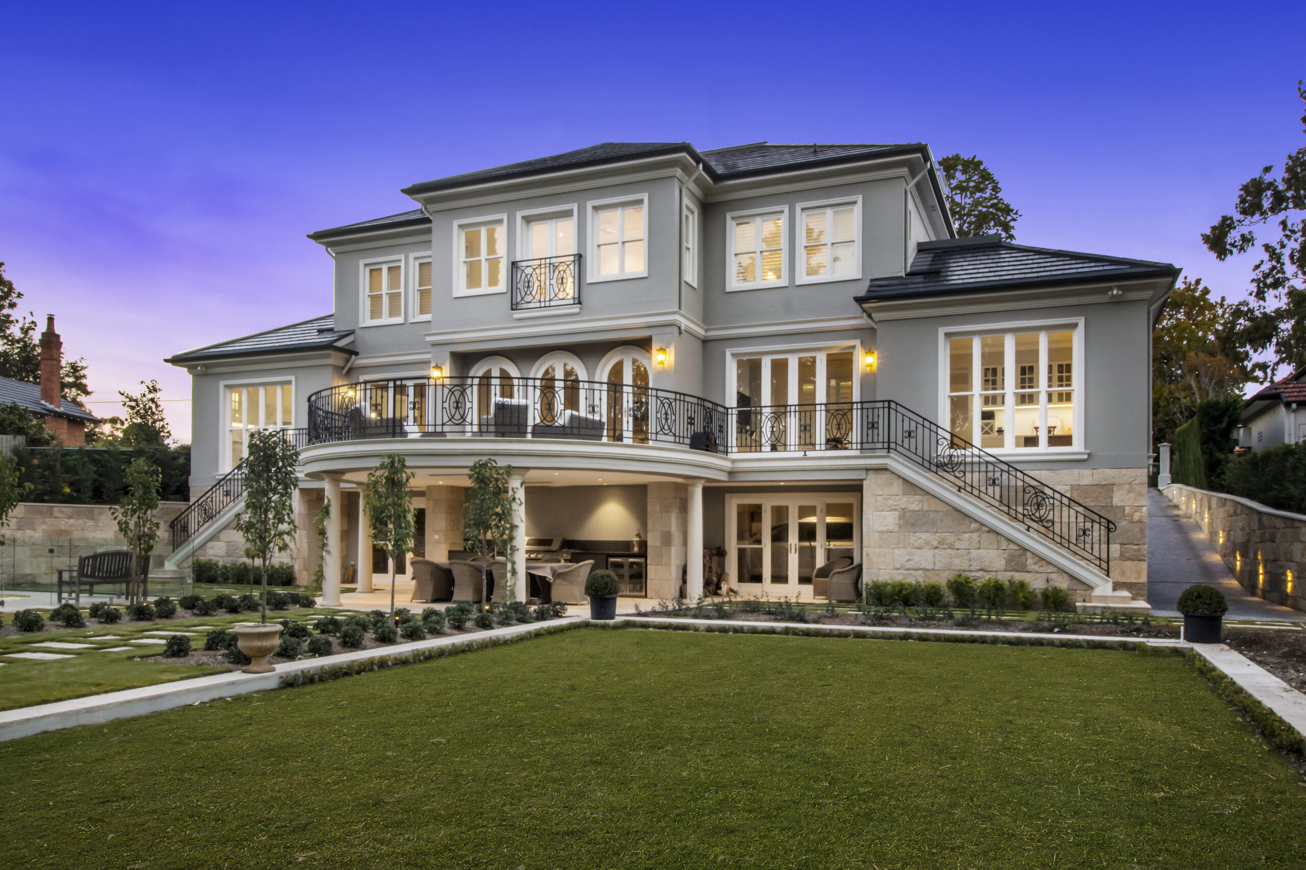 Dusk shot of an imposing French Provincial Home with manicured landscaping, sandstone foundations, wrought-iron balconies