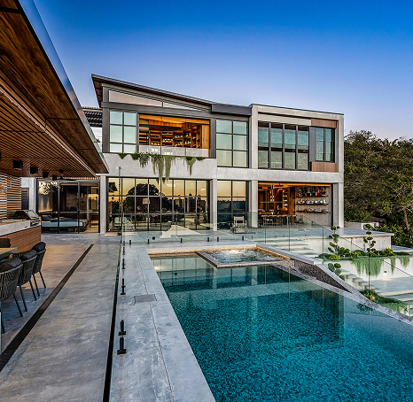 Dramatic lower view of a blue pool, surrounded by polished concrete; with the main house at the back