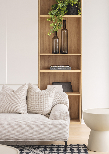 Timber bookcase set into the wall, against cream cabinetry. Styled with a luxuriously textured couch in front.
